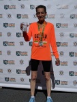 Photo of Celia after finishing a marathon first in her age group. She wears an orange shirt and has a medal
