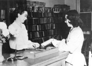 Librarian Marie Bracey and another woman look at a book at a circulation desk
