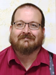 headshot of Mark Hall. He has brown hair and beard, and wears a maroon shirt with suspenders.