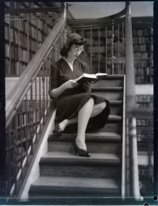 A woman in a black dress sits on the stairs reading a book